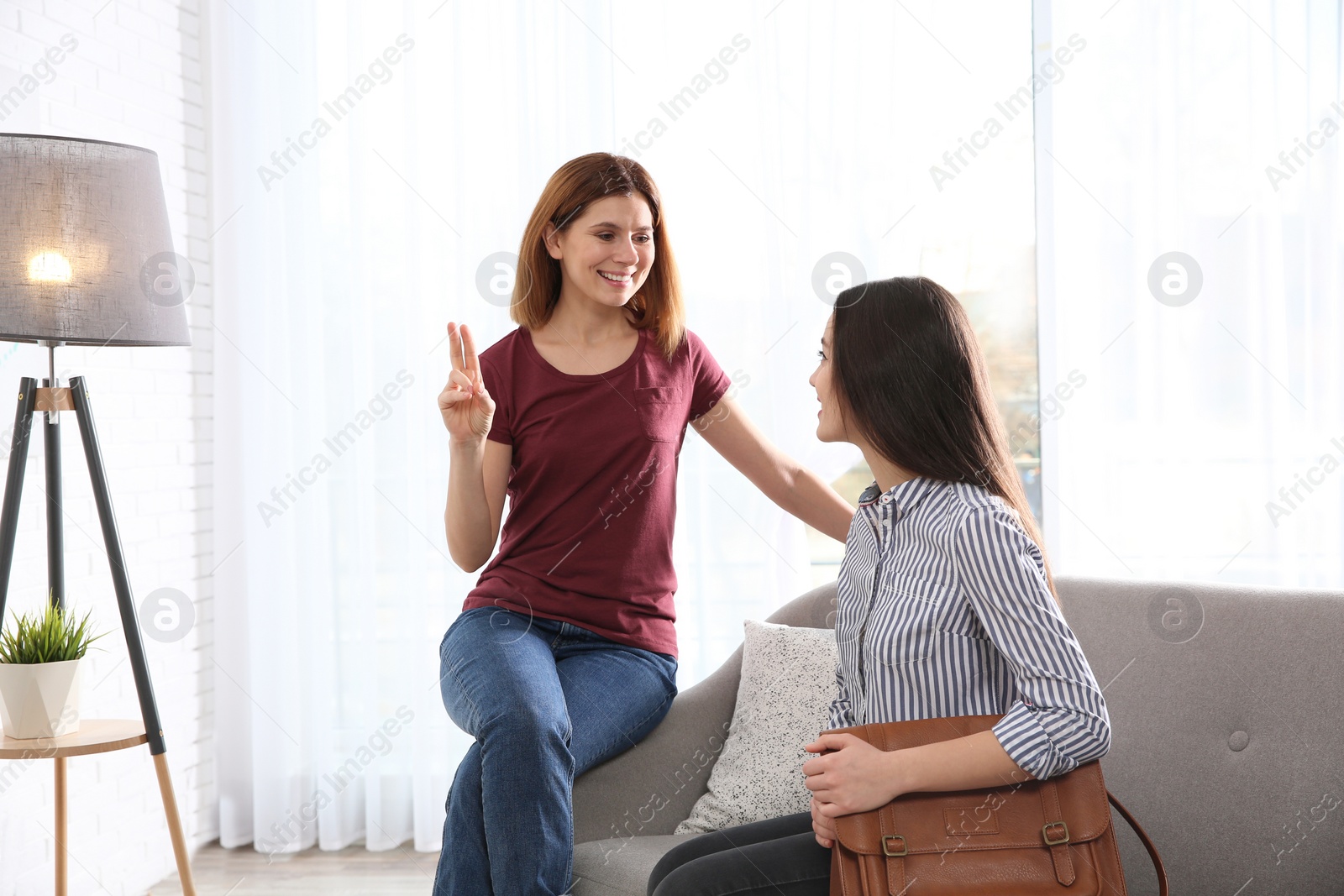 Photo of Hearing impaired friends using sign language for communication on sofa in living room