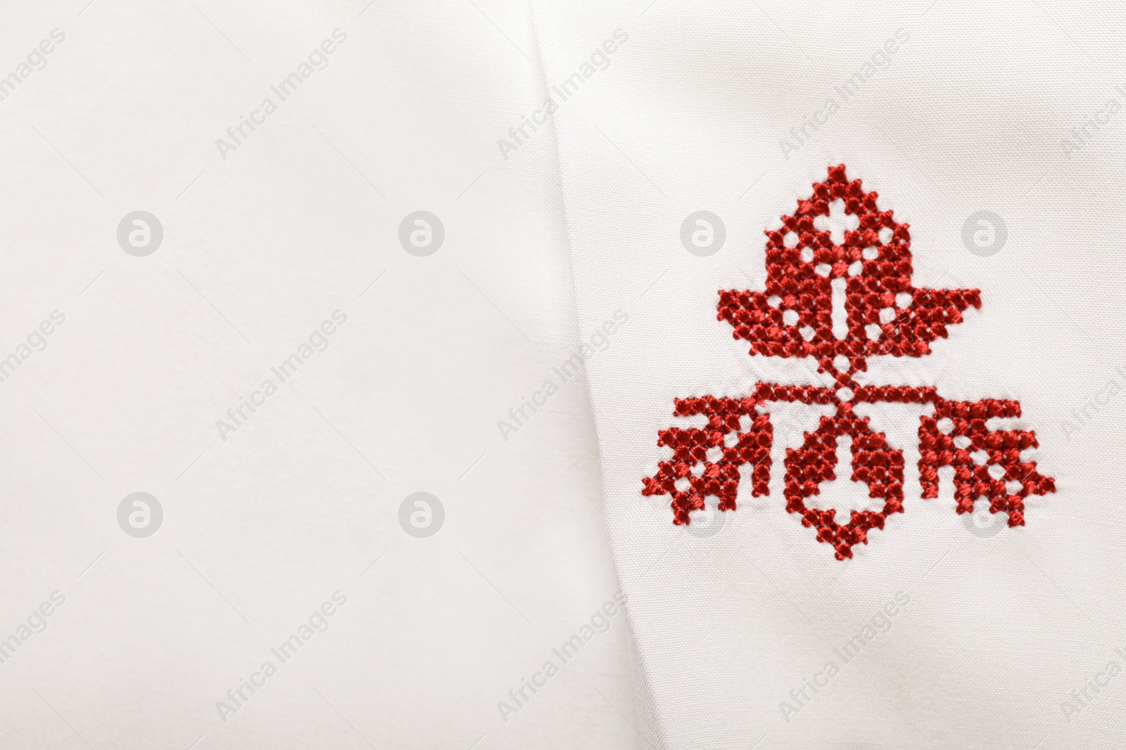 Photo of Beautiful red Ukrainian national embroidery on white fabric, top view. Space for text