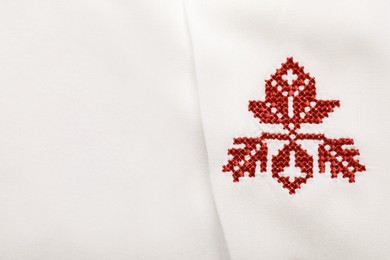 Photo of Beautiful red Ukrainian national embroidery on white fabric, top view. Space for text