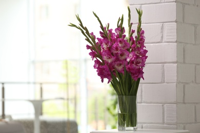 Vase with beautiful pink gladiolus flowers on wooden table in room, space for text