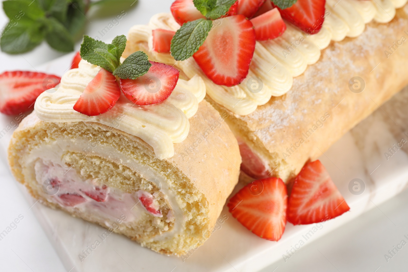 Photo of Delicious cake roll with strawberries and cream on white table, closeup