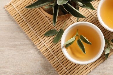 Photo of Aromatic sage tea and fresh leaves on wooden table, flat lay. Space for text