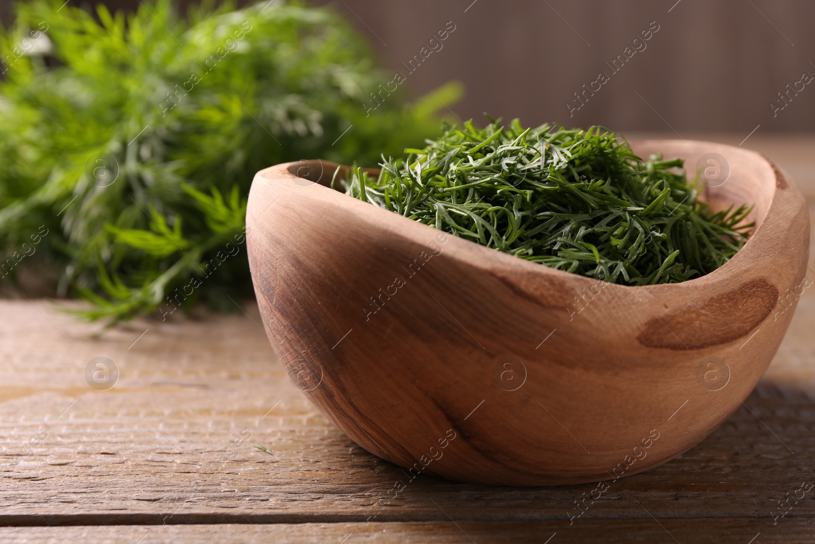 Photo of Fresh cut dill in bowl on wooden table, closeup