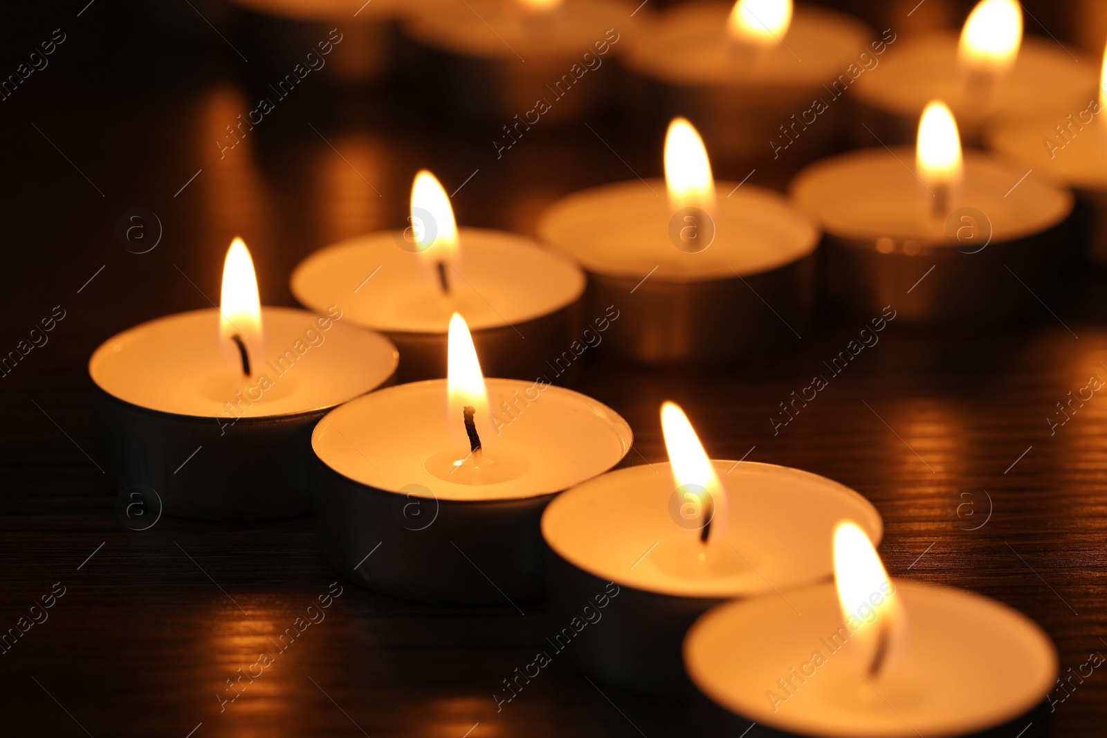 Photo of Burning tealight candles on dark surface, closeup