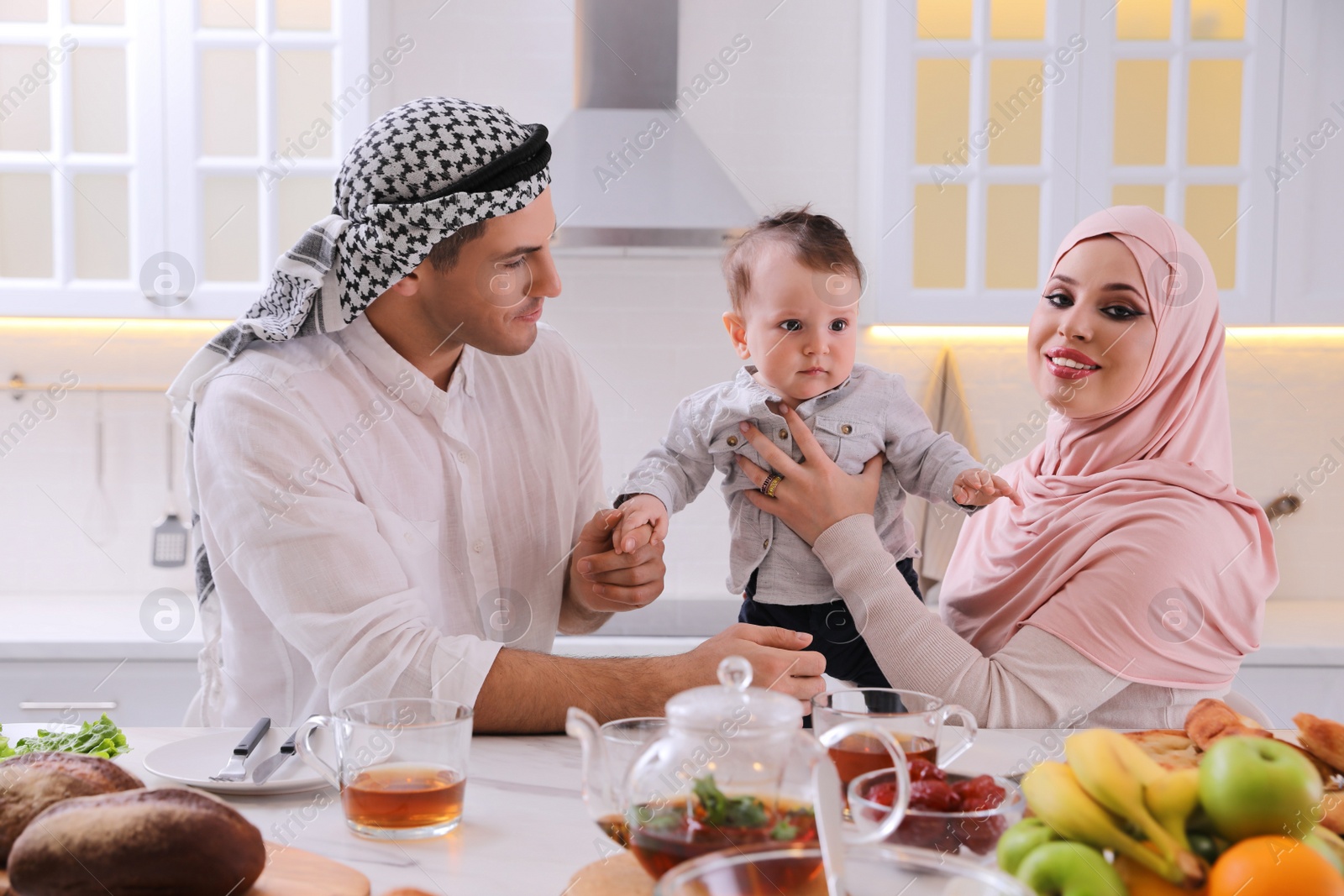 Photo of Happy Muslim family with little son at served table in kitchen