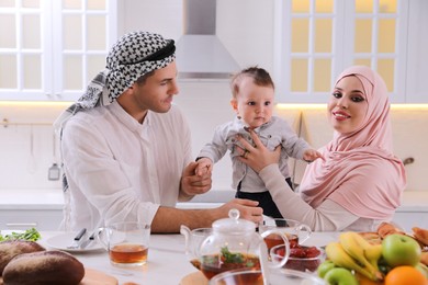 Happy Muslim family with little son at served table in kitchen
