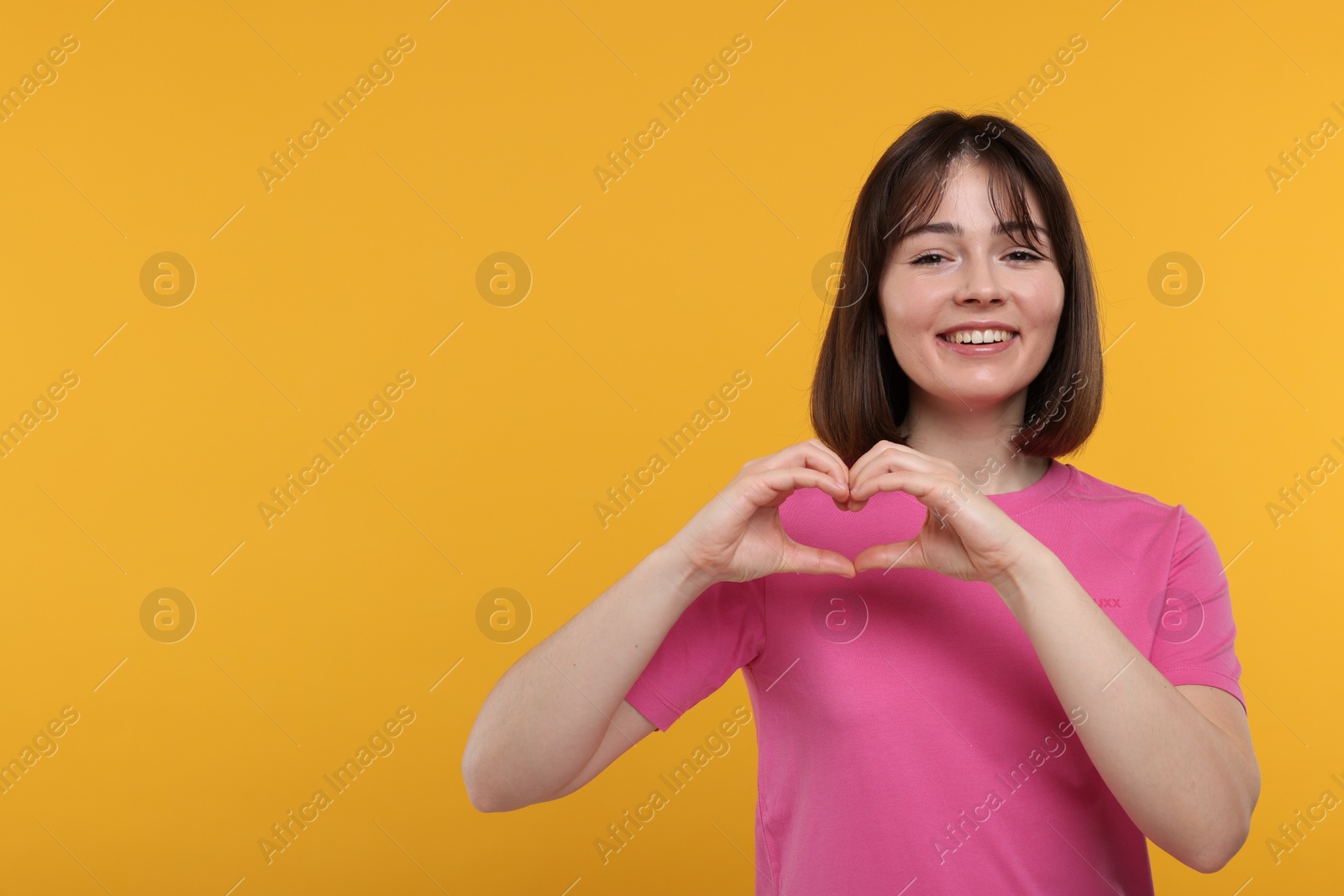 Photo of Happy woman showing heart gesture with hands on orange background, space for text