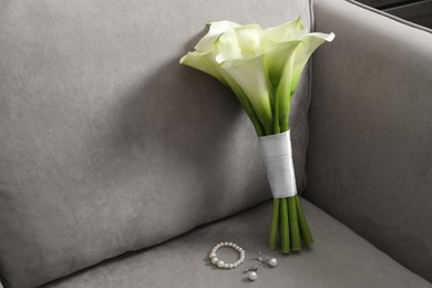 Photo of Beautiful calla lily flowers tied with ribbon and jewelry on sofa