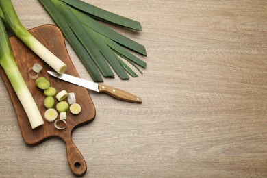 Photo of Fresh raw leeks and knife on wooden table, flat lay. Space for text