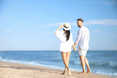 Happy young couple walking at beach on sunny day