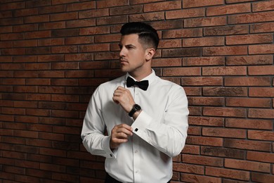 Photo of Handsome stylish man putting on cufflink near brick wall