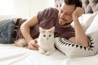 Photo of Young man with cute cat on bed at home