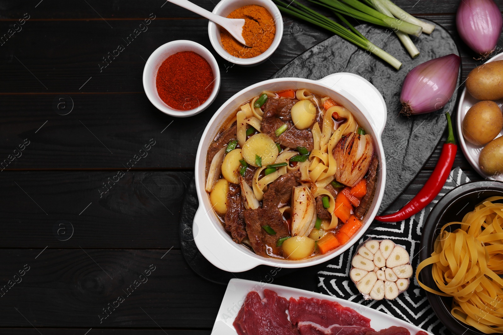 Photo of Pot of delicious vegetable soup with meat, noodles and ingredients on black wooden table, flat lay. Space for text