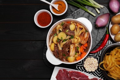 Photo of Pot of delicious vegetable soup with meat, noodles and ingredients on black wooden table, flat lay. Space for text