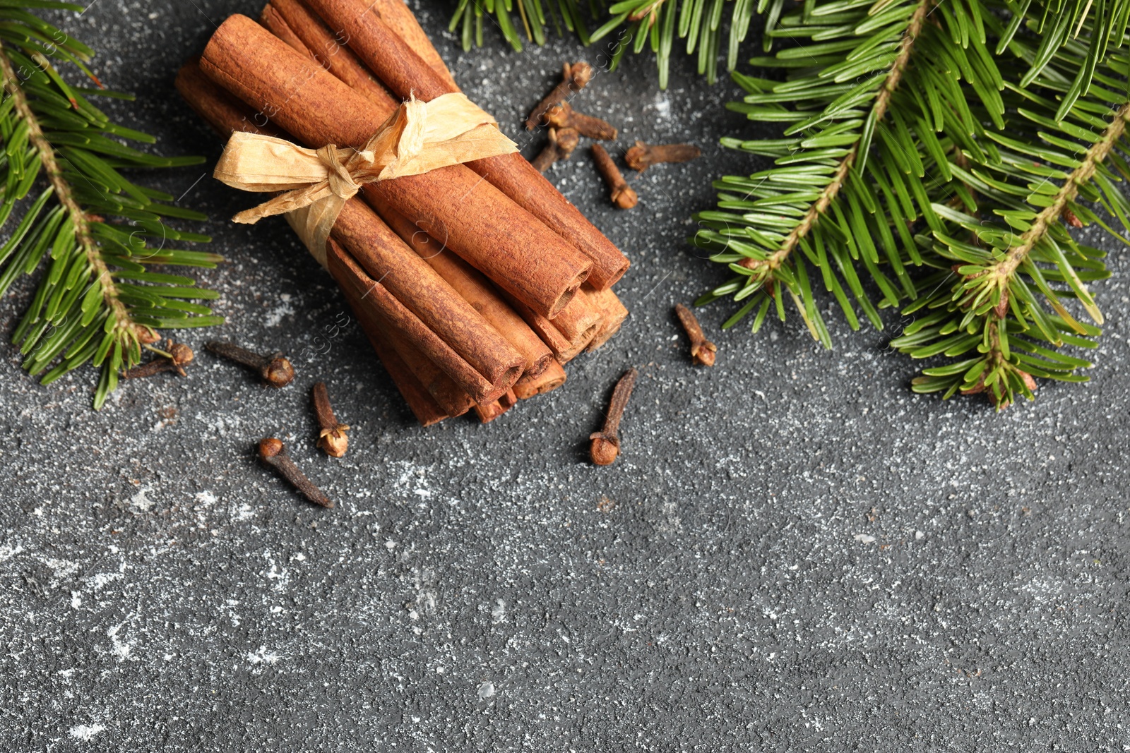 Photo of Different spices. Aromatic cinnamon sticks, clove seeds and fir branches on dark gray textured table, flat lay. Space for text