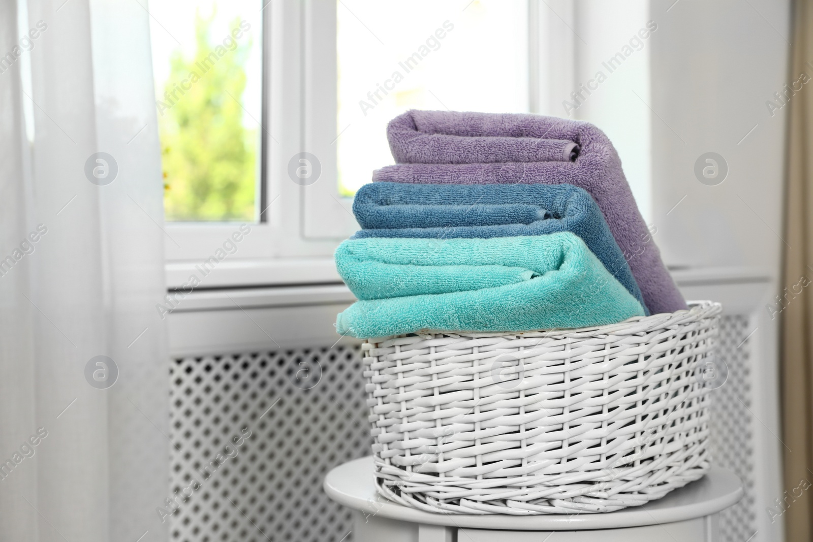 Photo of Basket with clean soft towels on table near window. Space for text