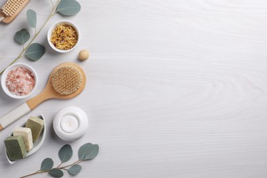 Flat lay composition with different spa products, burning candle and eucalyptus branches on light wooden table. Space for text