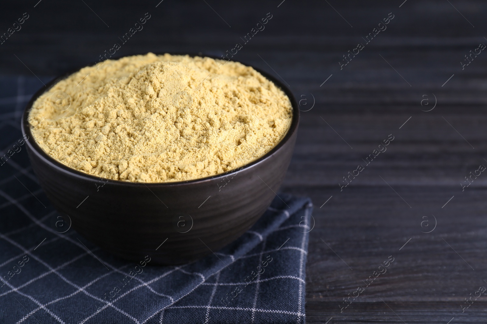 Photo of Bowl of aromatic mustard powder on black wooden table, closeup. Space for text