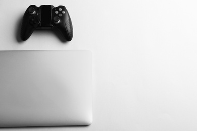 Photo of Video game controller and laptop on light background, top view with space for text