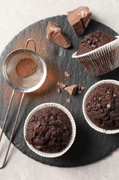 Delicious chocolate muffins and sieve with cocoa powder on light table, top view