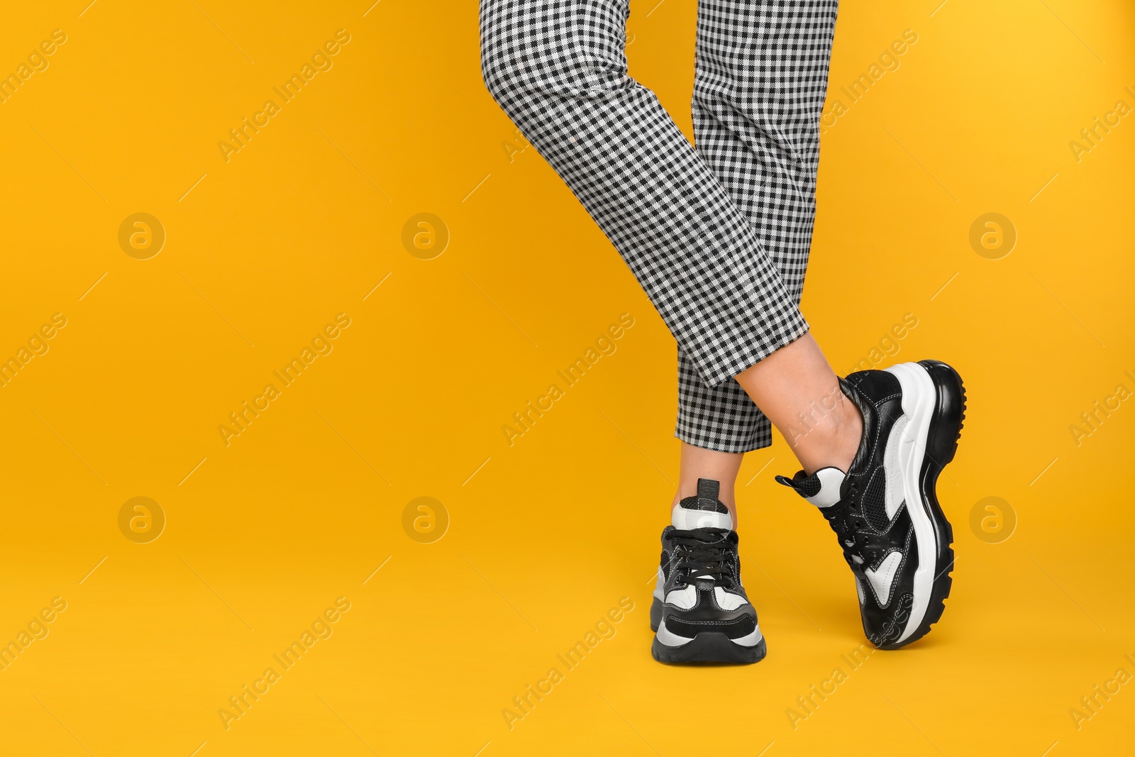 Photo of Woman wearing stylish sneakers on yellow background, closeup. Space for text