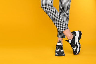 Photo of Woman wearing stylish sneakers on yellow background, closeup. Space for text