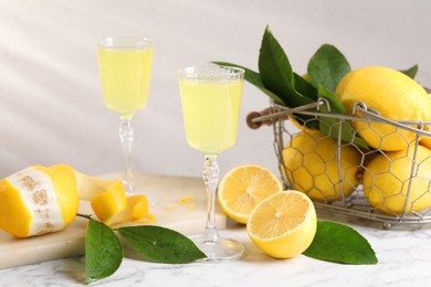 Photo of Tasty limoncello liqueur, lemons and green leaves on white marble table