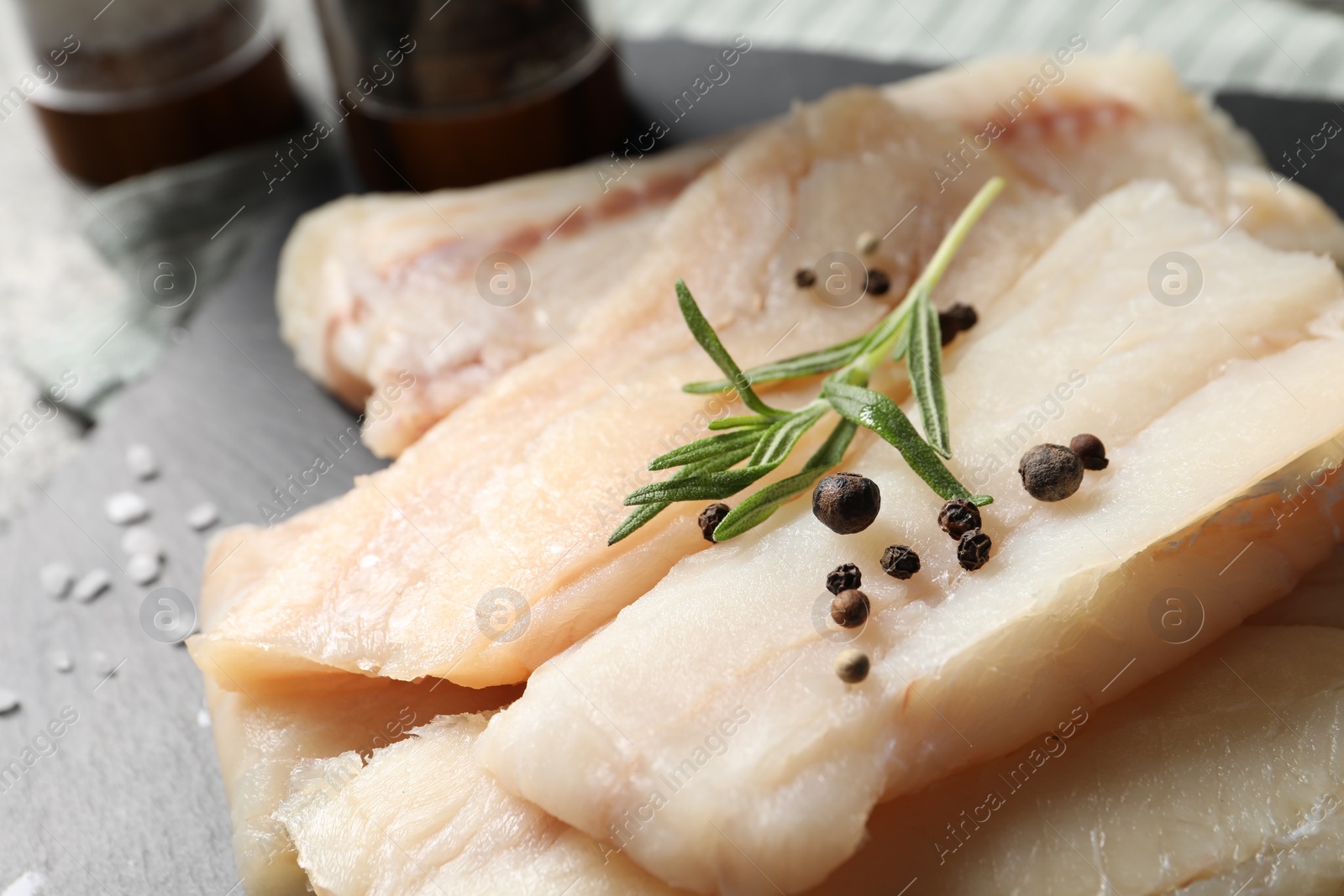 Photo of Pieces of raw cod fish, rosemary and peppercorns on table, closeup