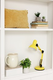 Shelves with lamp, books and different decor indoors. Interior design