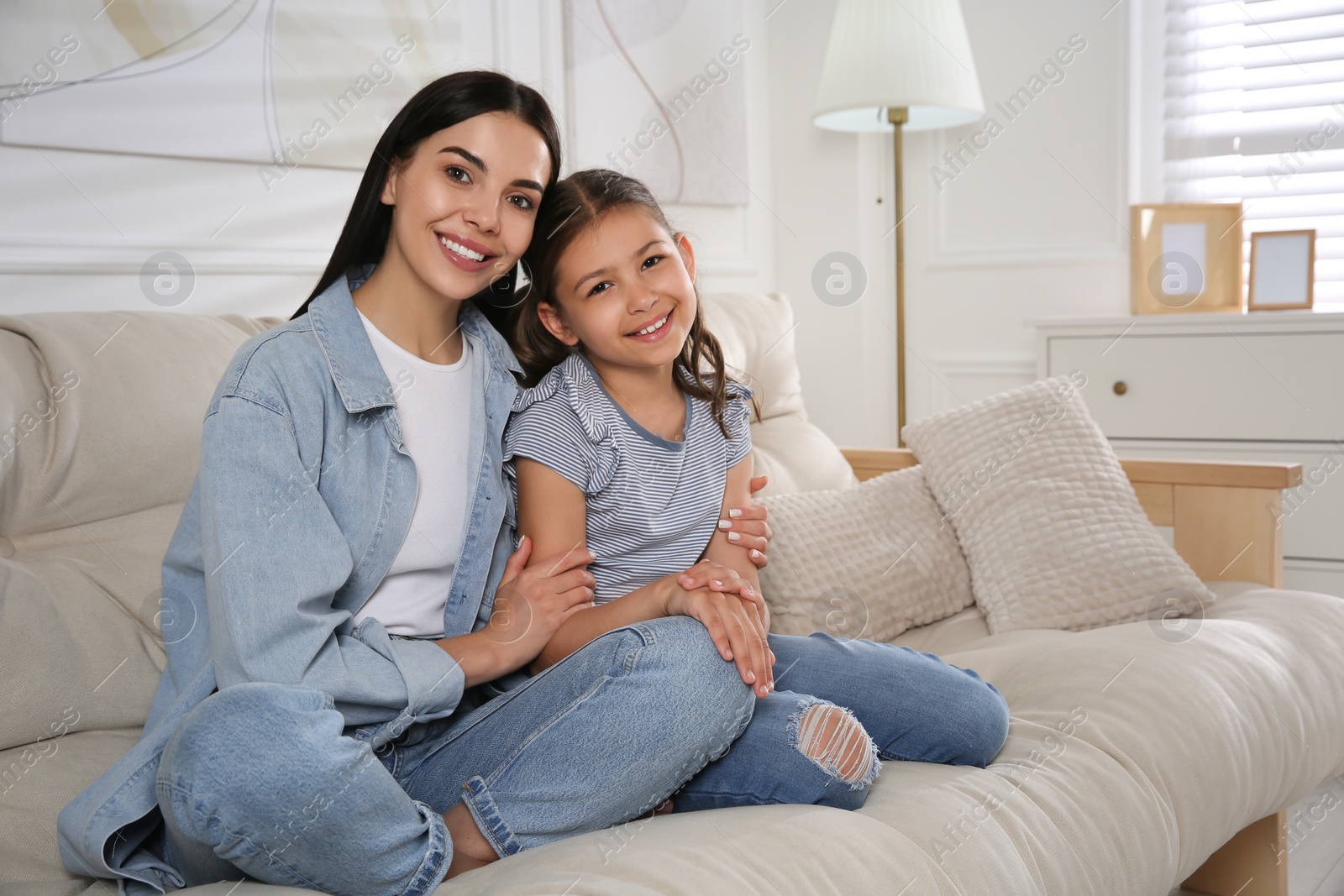 Photo of Young mother and her daughter on sofa in living room. Adoption concept