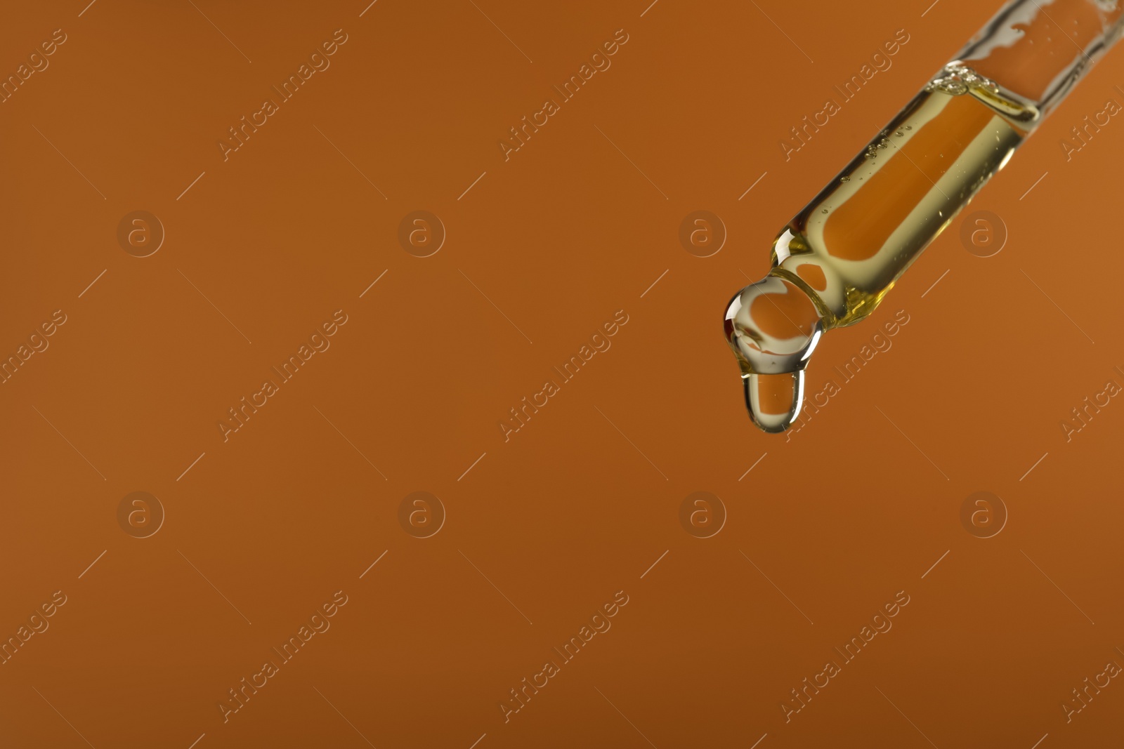 Photo of Dripping hydrophilic oil from pipette on brown background, closeup. Space for text