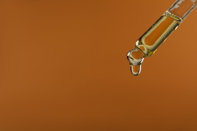 Photo of Dripping hydrophilic oil from pipette on brown background, closeup. Space for text