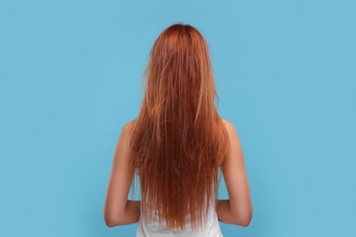 Woman with damaged messy hair on light blue background, back view