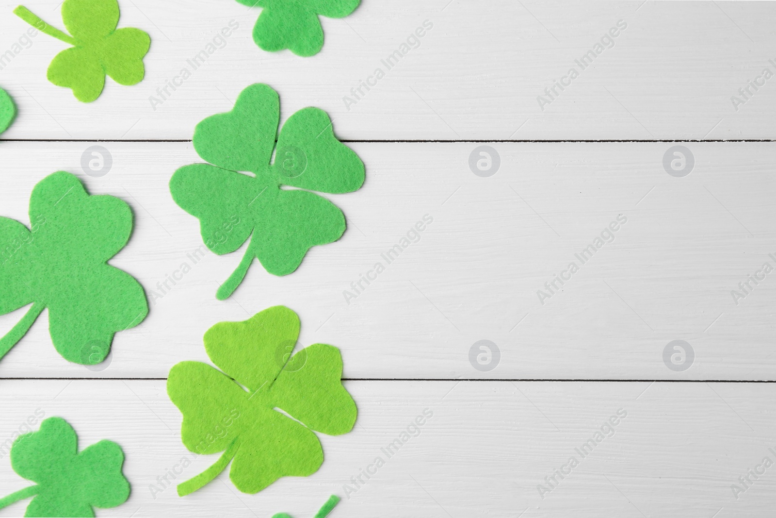 Photo of St. Patrick's day. Decorative green clover leaves on white wooden table, flat lay. Space for text