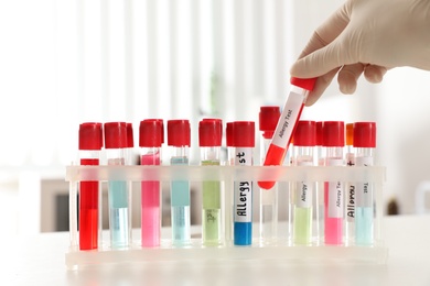 Doctor holding tube with label ALLERGY TEST over table, closeup