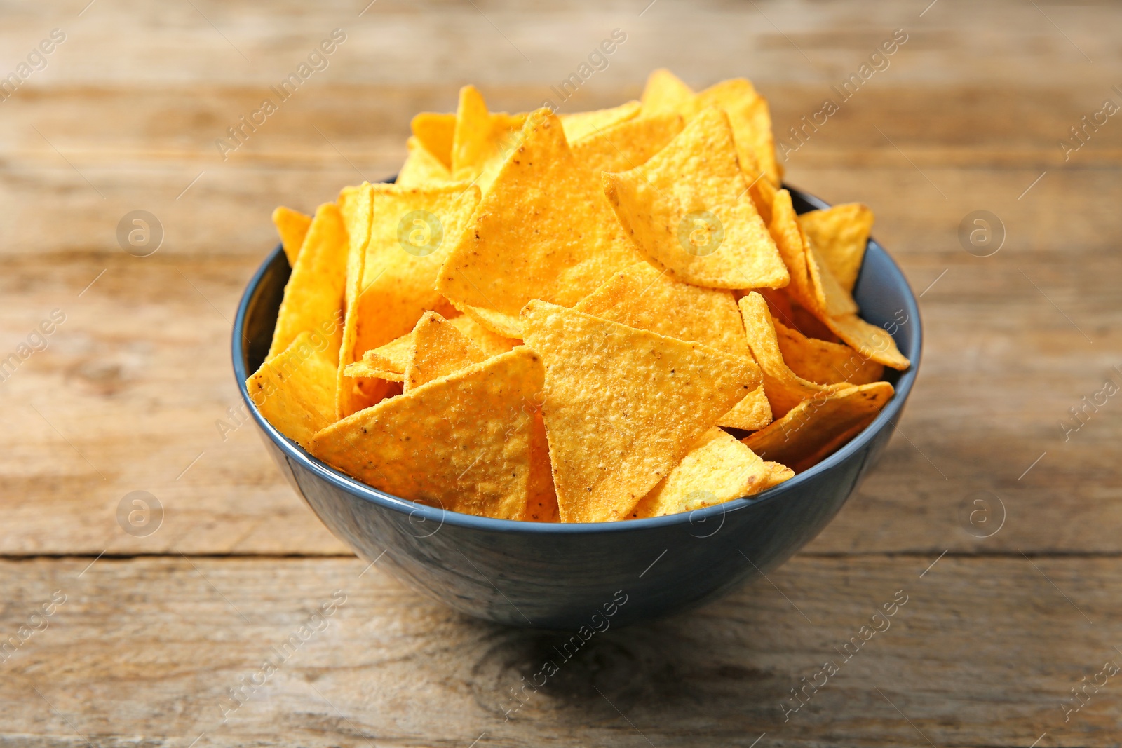 Photo of Tasty mexican nachos chips in color bowl on wooden table