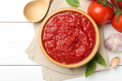 Photo of Homemade tomato sauce in bowl, spoon and fresh ingredients on white wooden table, flat lay