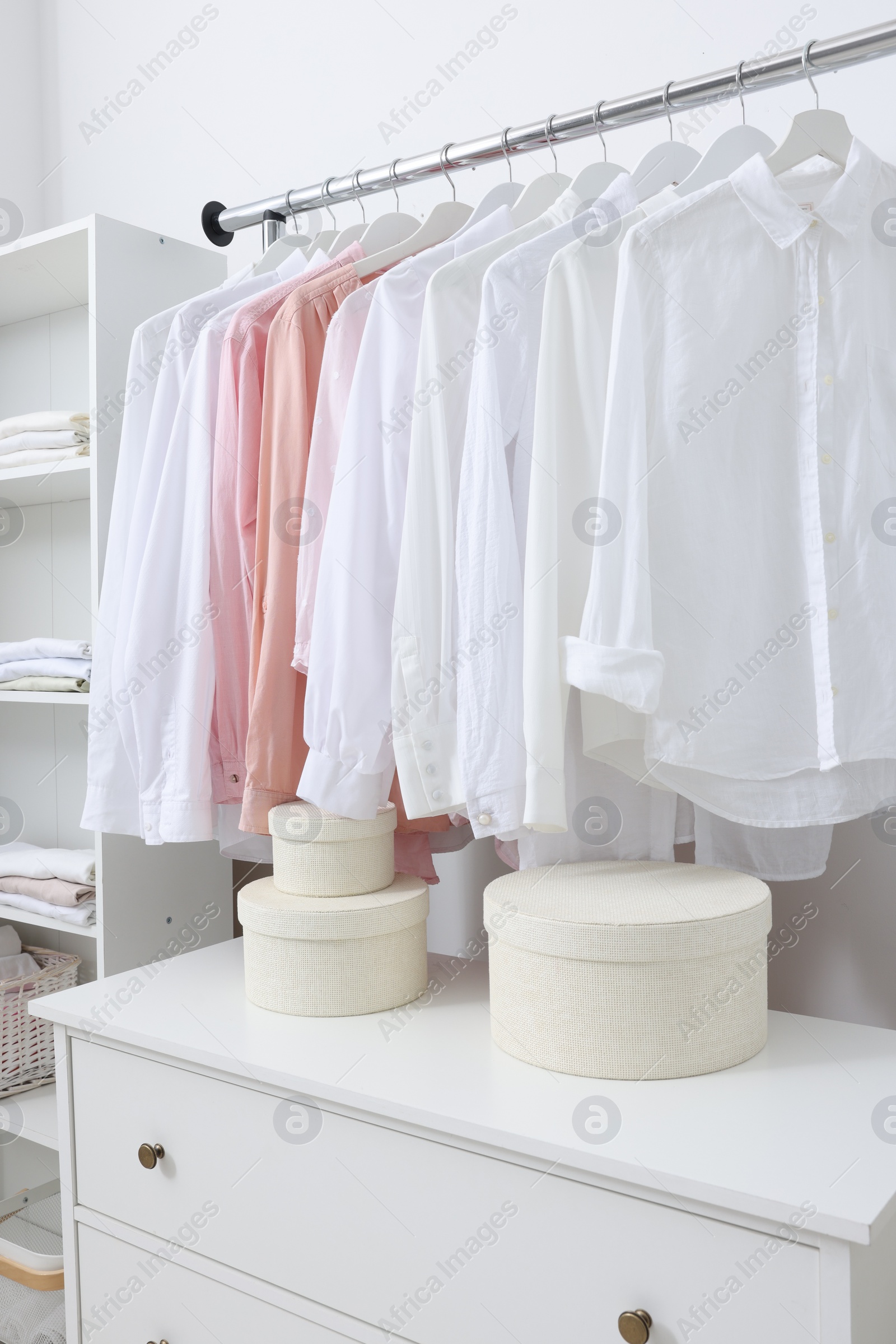 Photo of Wardrobe organization. Rack with different stylish clothes and chest of drawers indoors