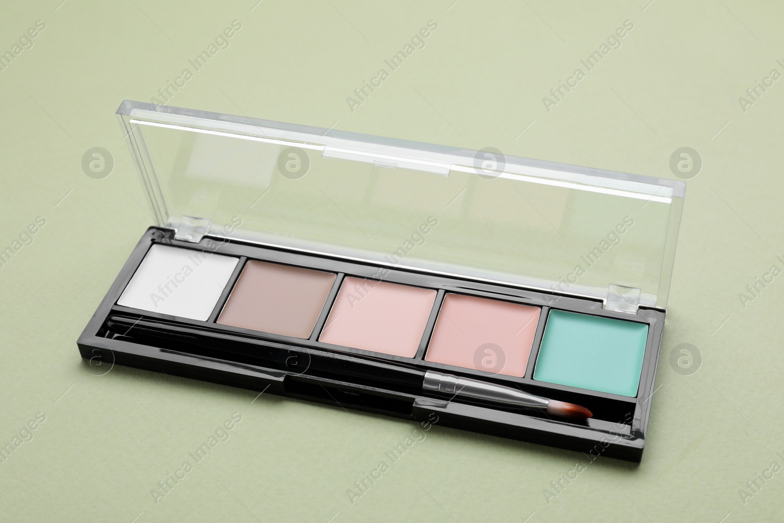 Photo of Colorful contouring palette with brush on pale green background, closeup. Professional cosmetic product