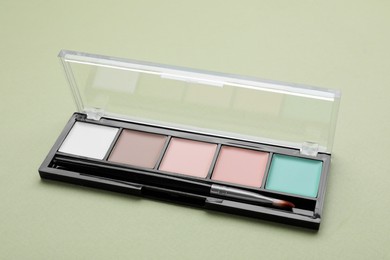Photo of Colorful contouring palette with brush on pale green background, closeup. Professional cosmetic product