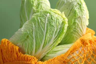 Photo of Fresh Chinese cabbages in string bag on green background, closeup