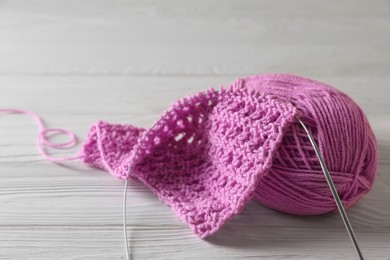 Photo of Soft pink yarn, knitting and metal needle on white wooden table, closeup