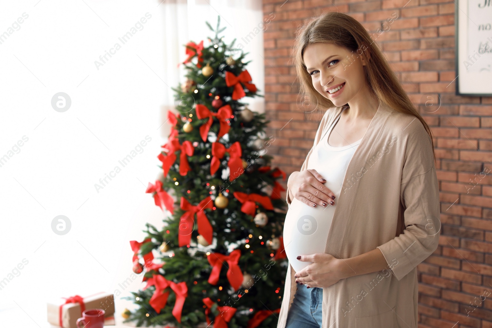 Photo of Pregnant woman near Christmas tree at home. Expecting baby