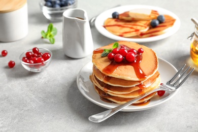 Stack of tasty pancakes with berries and syrup on table