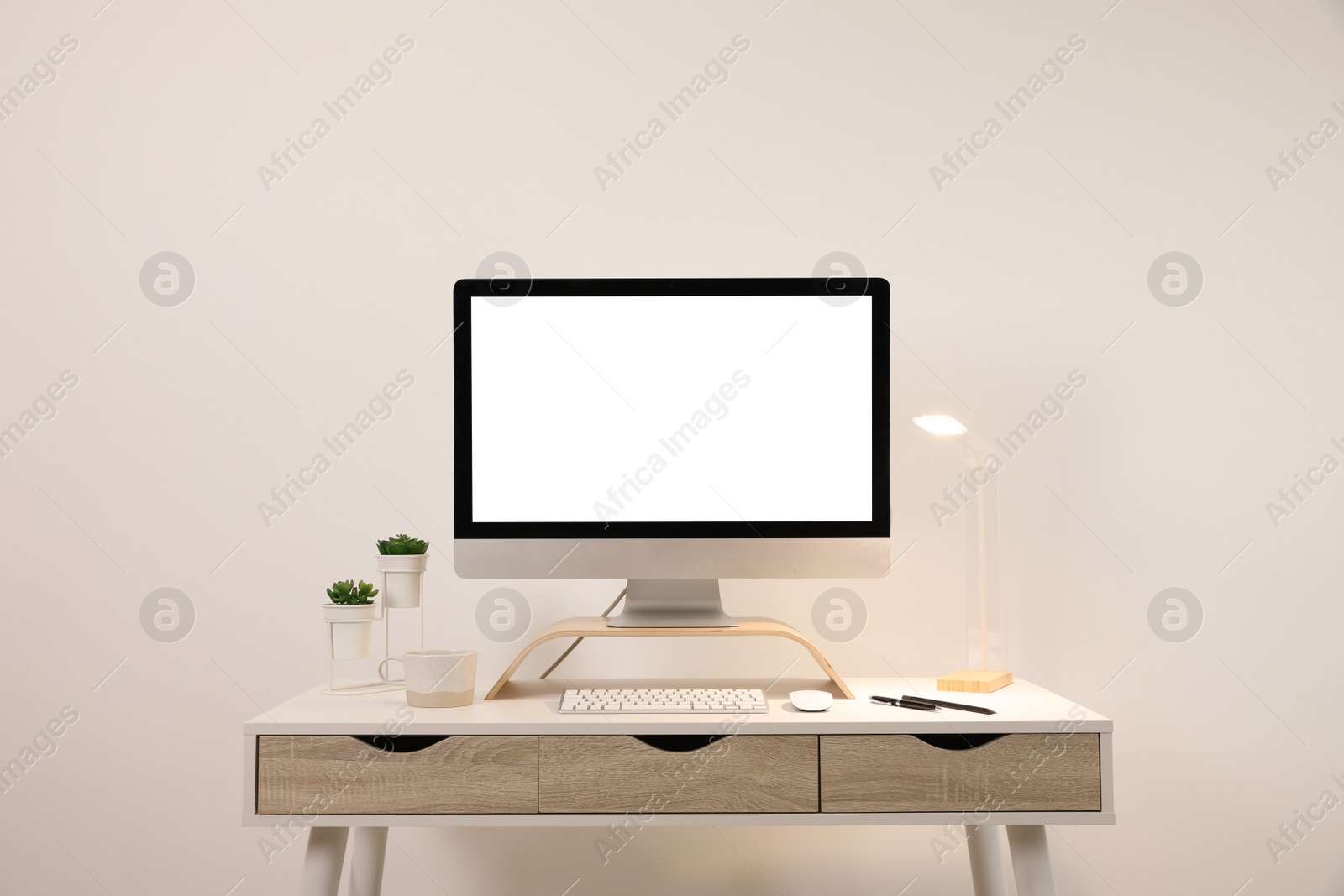 Photo of Comfortable workplace with blank computer display on desk near light wall. Space for text