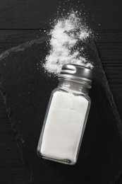 Photo of Salt shaker on black wooden table, top view