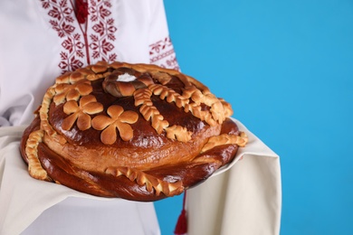 Photo of Woman with korovai on light blue background, closeup. Ukrainian bread and salt welcoming tradition