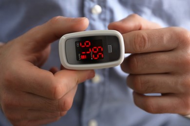 Photo of Man measuring oxygen level with modern fingertip pulse oximeter, closeup