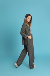 Full length portrait of beautiful young woman in fashionable suit on light blue background. Business attire