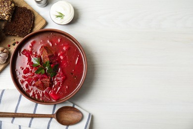 Photo of Stylish brown clay bowl with Ukrainian borsch served on white wooden table, flat lay. Space for text